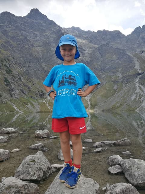 Leon w koszulce ze schroniskiem Morskie Oko, w tle skalne ściany nad stawem