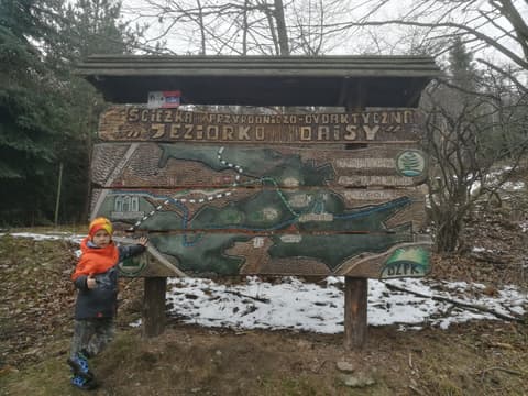 Leon przy drewnianej tablicy ścieżki do Jeziorka Daisy