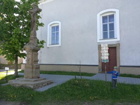 Leon przy drogowskazach obok wiejskiego kościoła i kamiennej figury