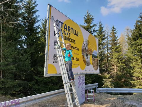 Leon na drabinie przy billboardzie Biegu Piastów