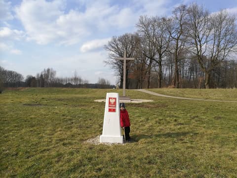 Leon przy słupku granicznym z orłem, w tle drewniany krzyż